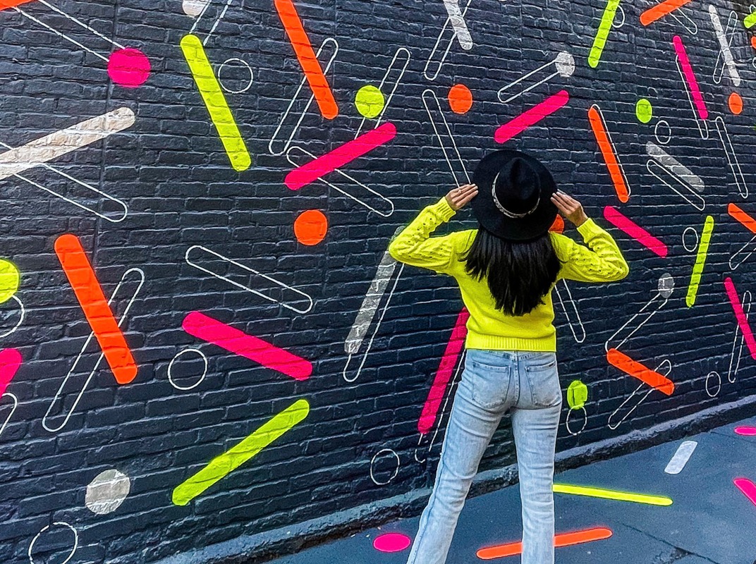 Heather in a yellow sweater in front of a neon confetti mural